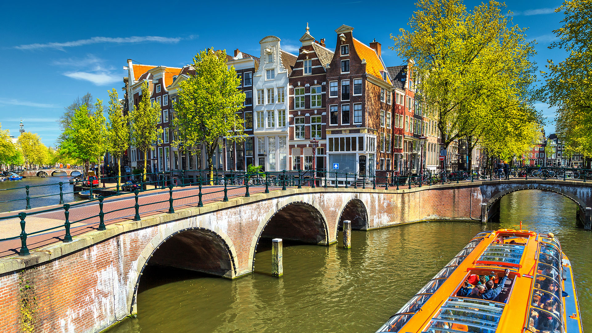 Canal tour boat passing a brick bridge and gabled houses in Amsterdam